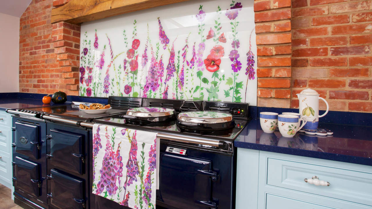 Bright floral glass bespoke splashbacks with poppies and foxgloves behind an Aga in a blue country kitchen