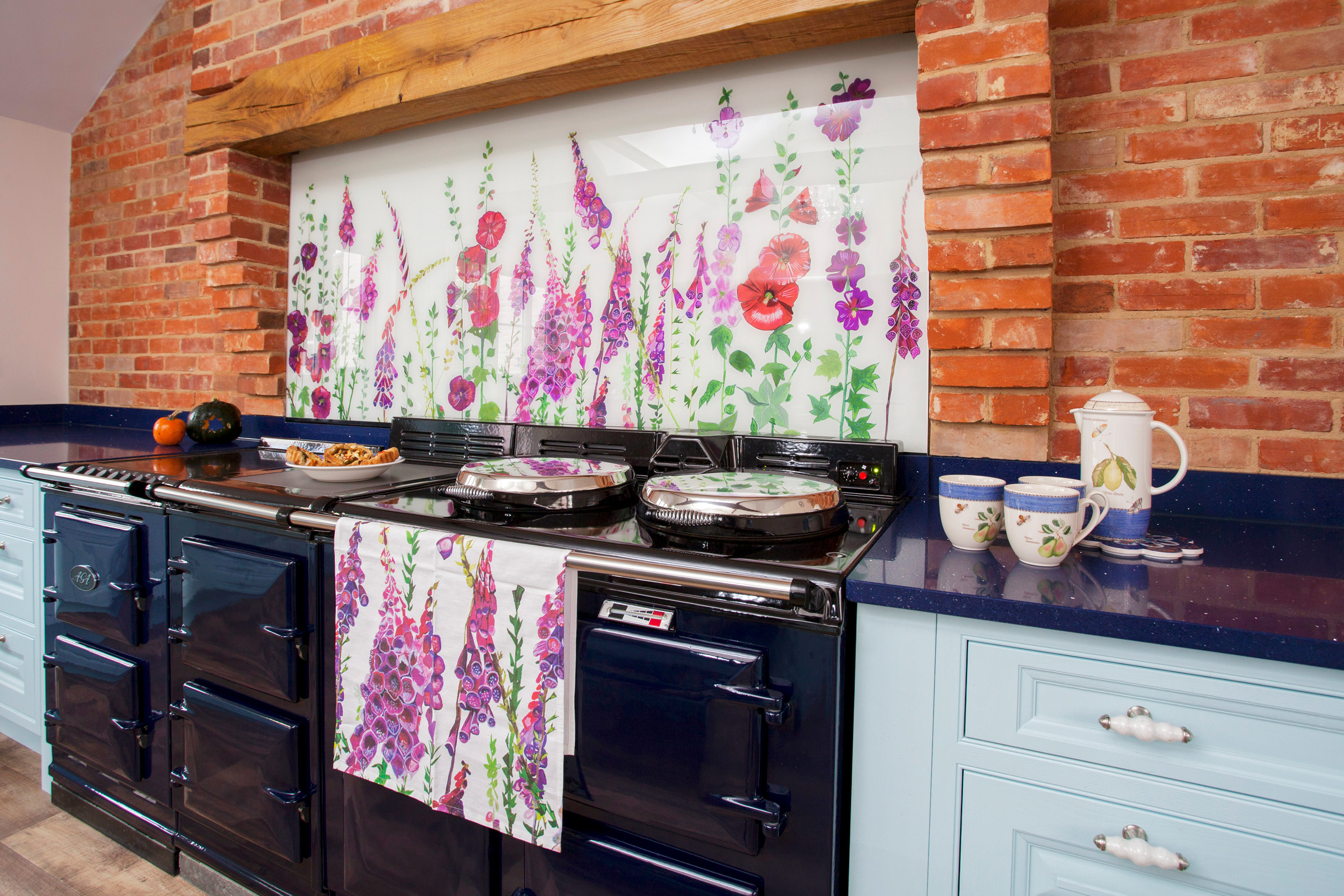 Bright floral glass bespoke splashbacks with poppies and foxgloves behind an Aga in a blue country kitchen